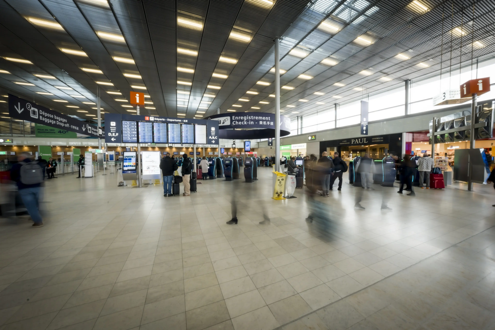 Busy airport hall with check-in kiosks, passenger flow and directional signage.