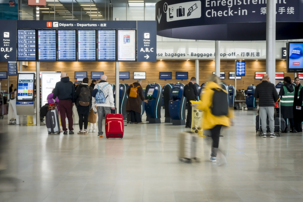 Airport hall with self‑service check‑in kiosks and passengers moving through departure areas.