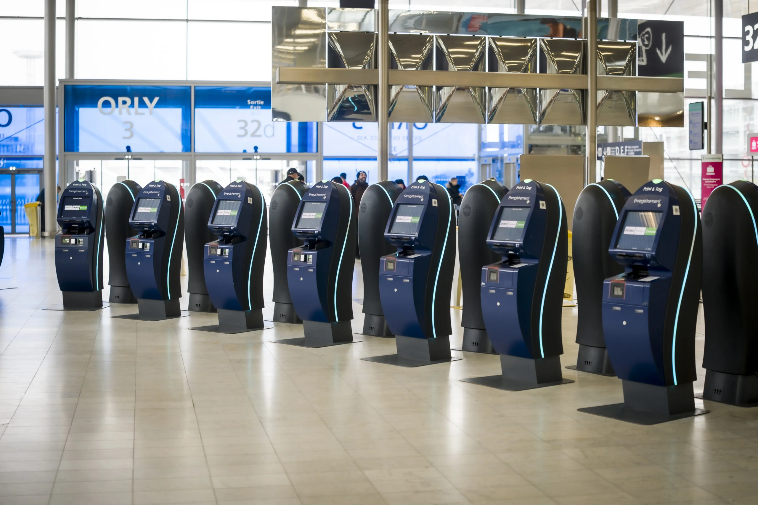 Row of self‑service check‑in kiosks in an airport hall with illuminated interfaces.