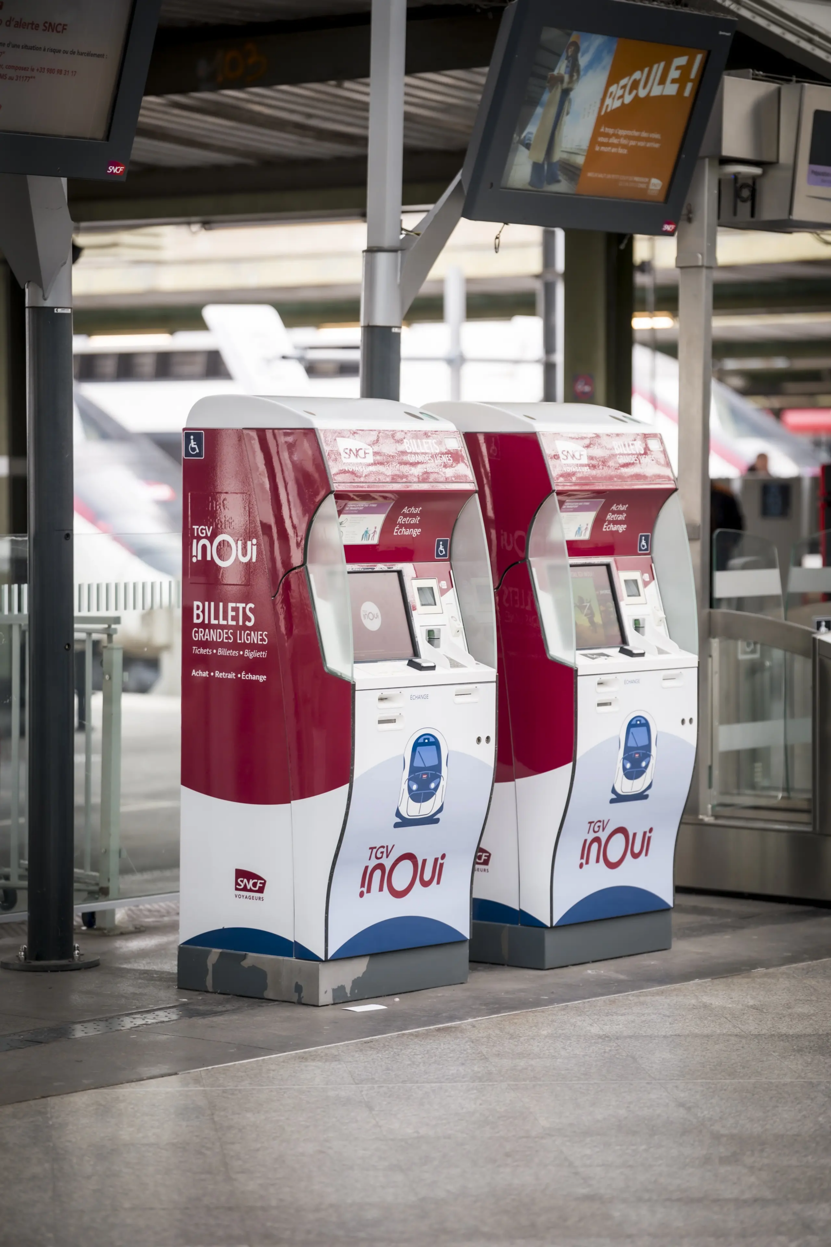 Bornes de billetterie en libre-service sur quai de transport terrestre avec interface utilisateur.