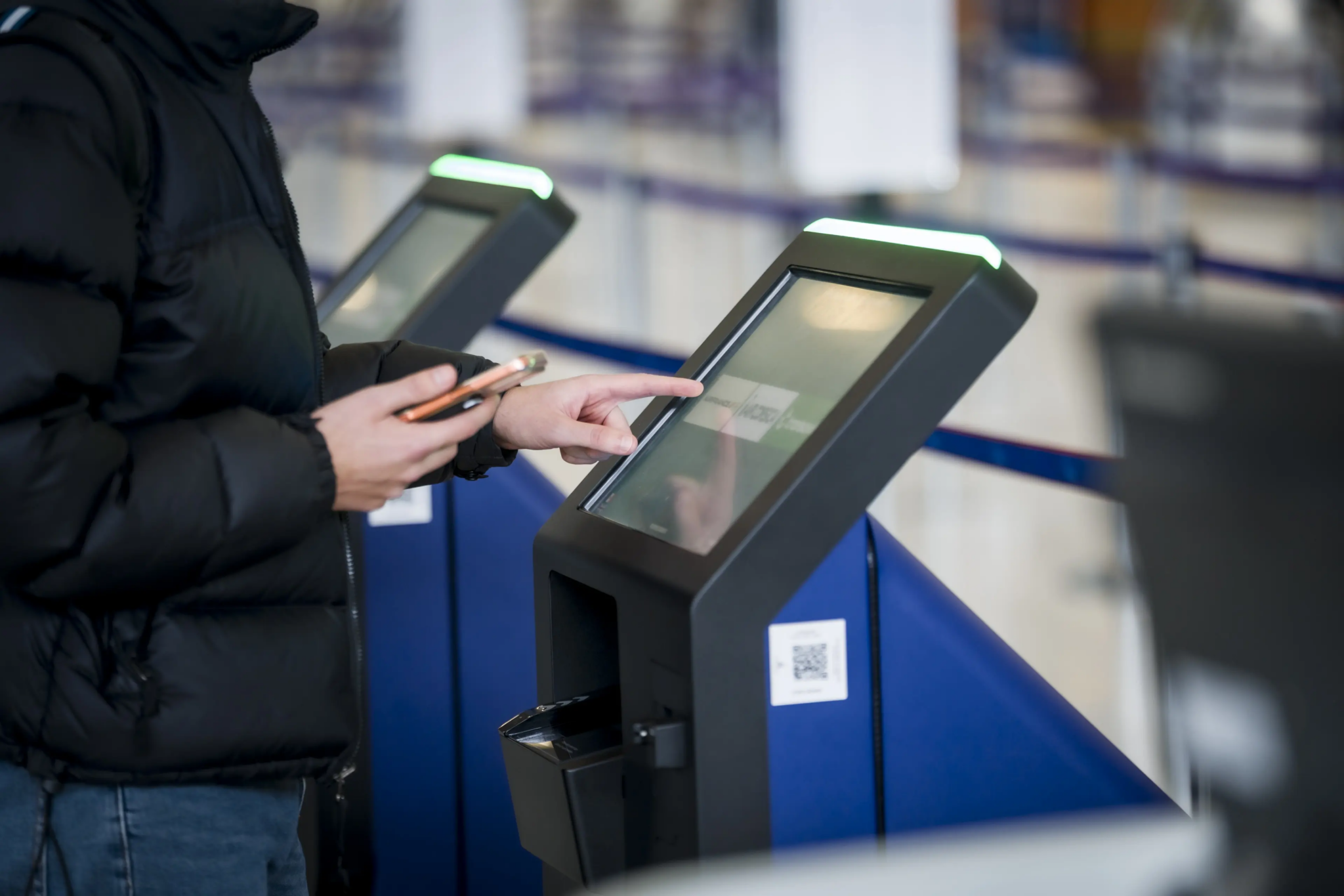 User interacting with a self‑service touchscreen kiosk in an air transport area.
